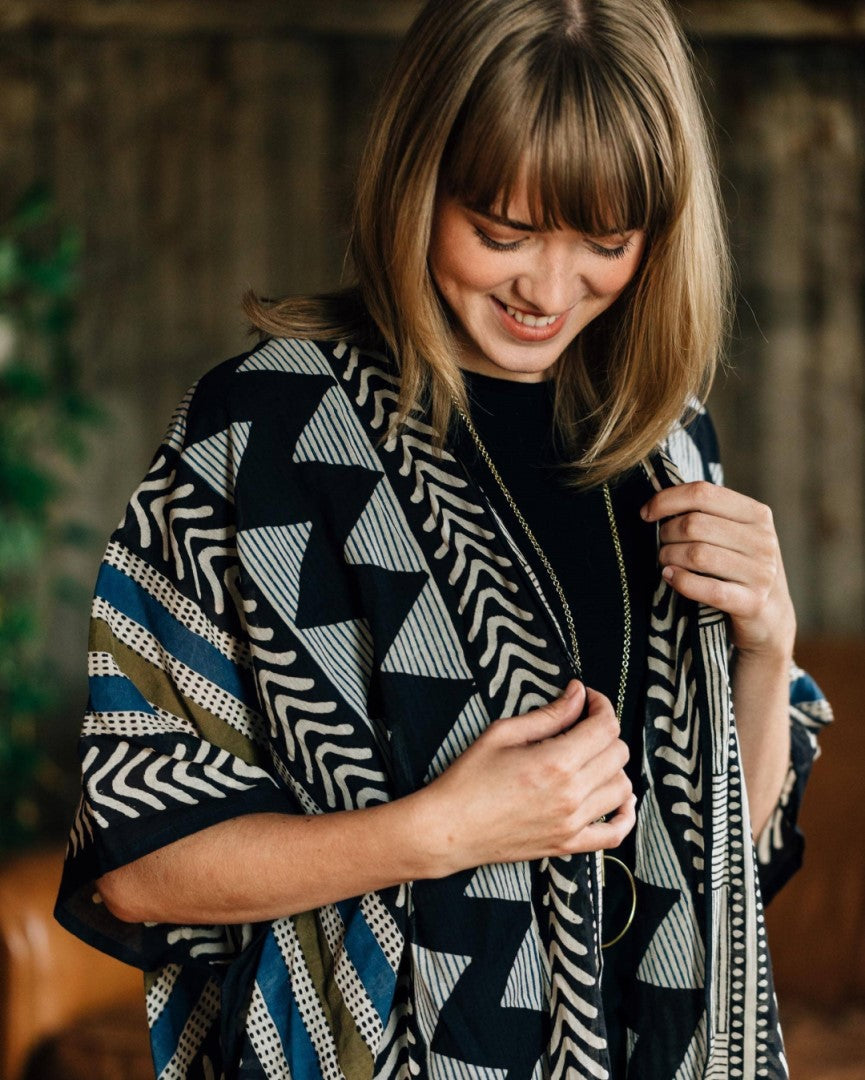 A blond woman with bangs looks lovingly at a black, white, blue, and green cardigan.