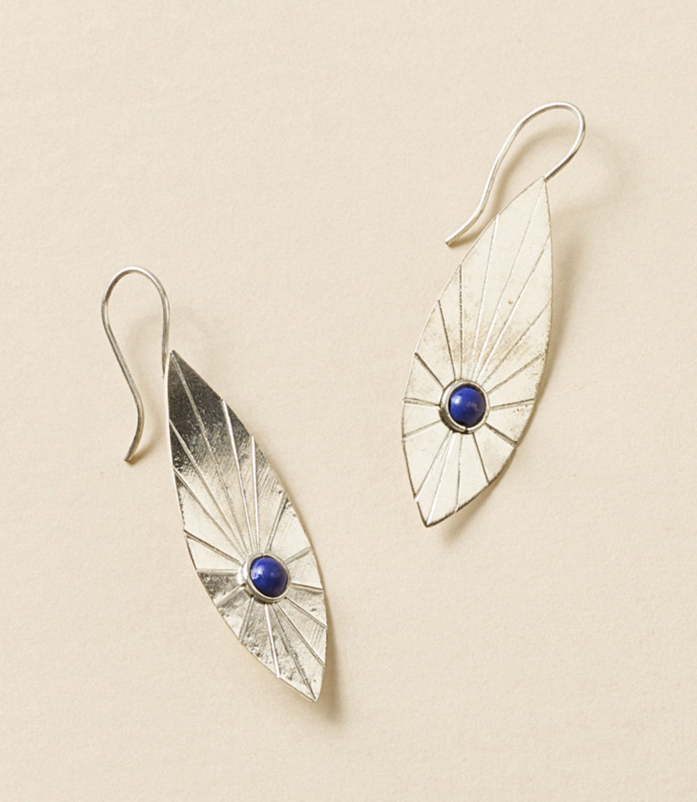 Two silver leaf-shaped earrings with blue stone accents on a beige background.
