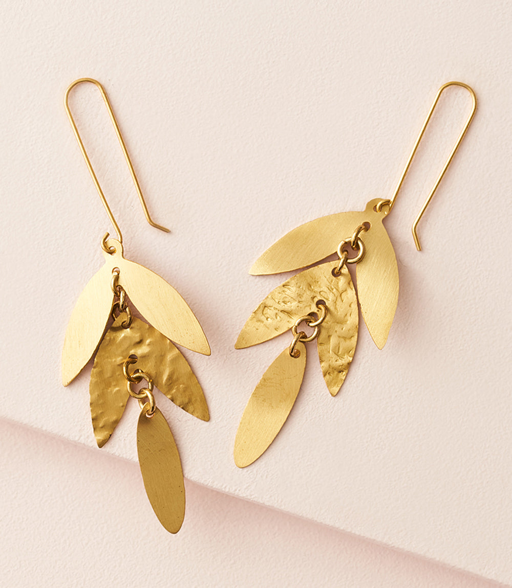 Two gold chandelier-style earrings on a soft pink background.