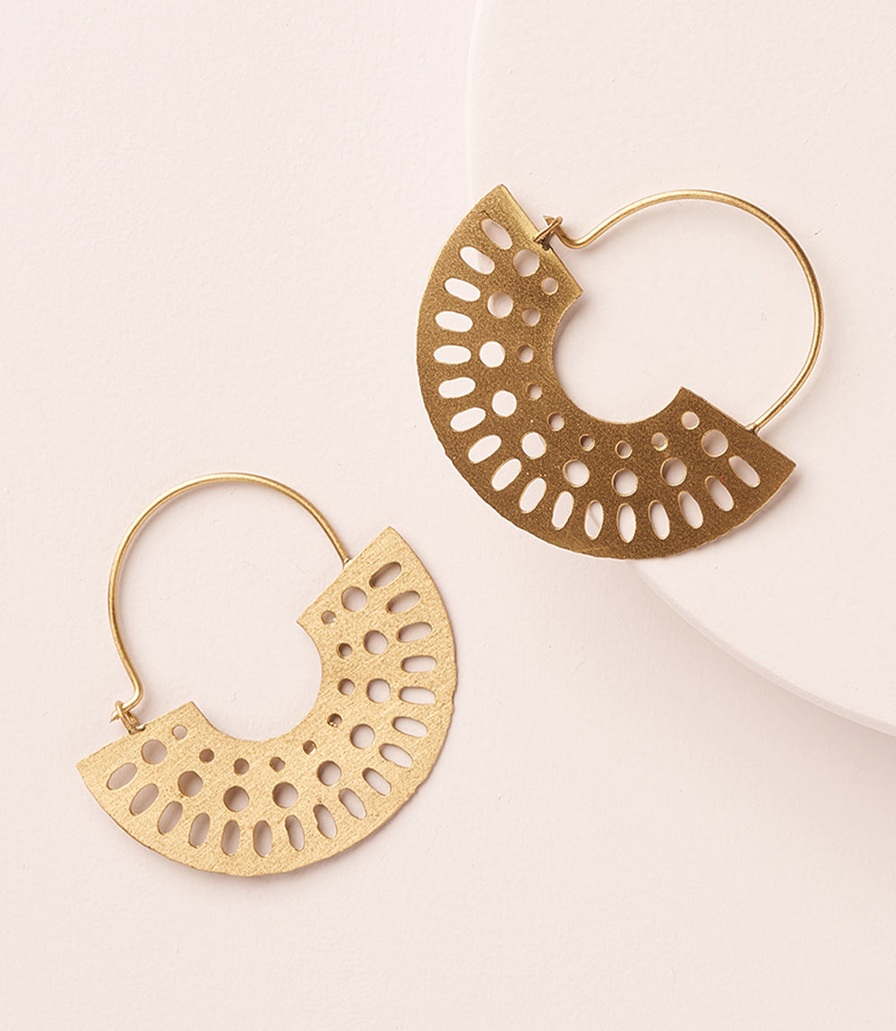 Two gold hoop earrings with artful cutouts lay on a dressing table.