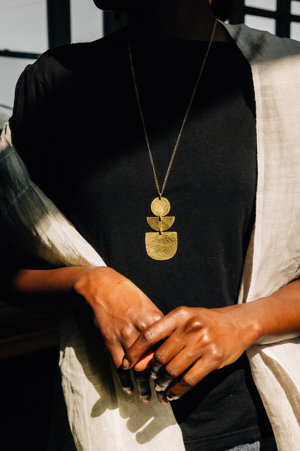 A geometric gold necklace is worn by a woman with a black turtleneck.