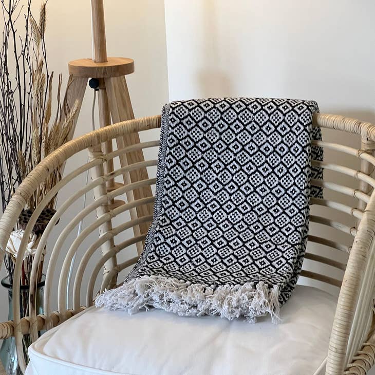 Black and white decorative cotton throw sits on a rattan chair