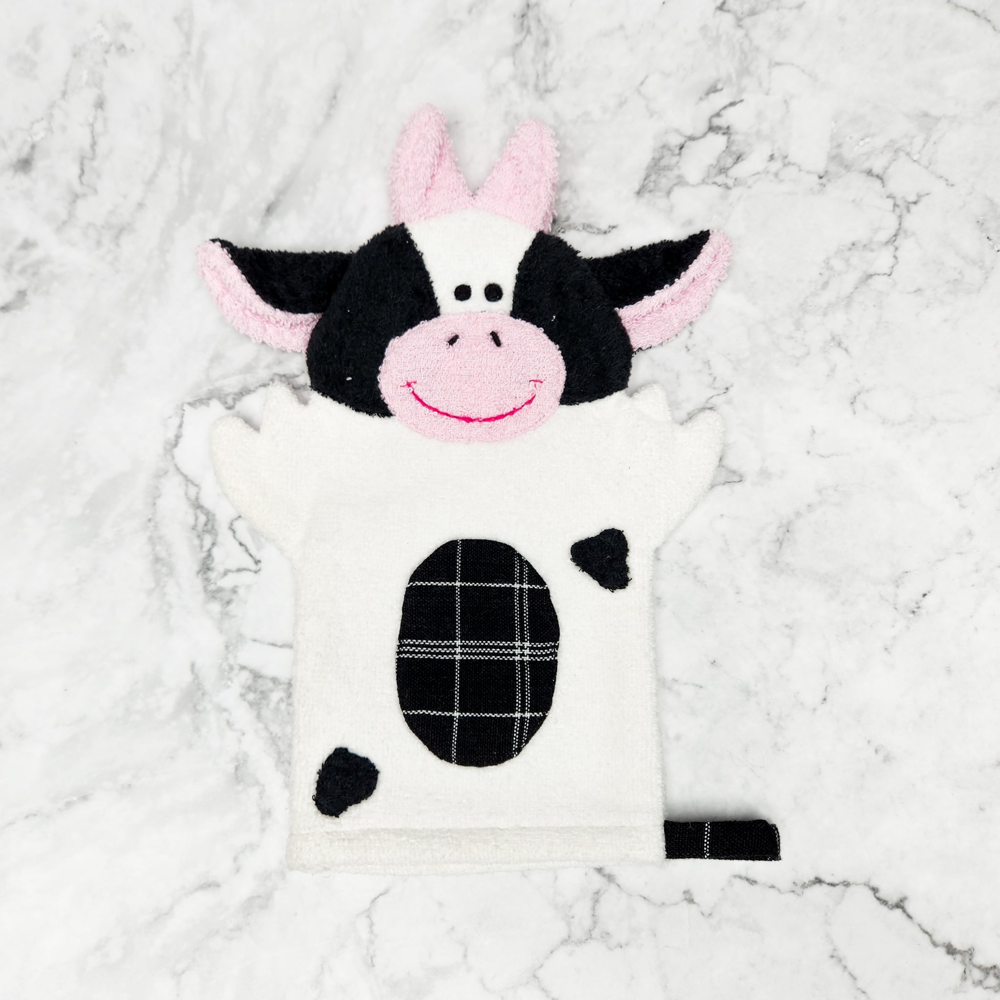 Photo shows a cow puppet washcloth, white cow body with black spots and face, with cute smile